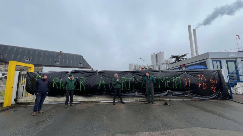 Photo of FDSEA leaders and young farmers in front of the Danone factory in Ferrière-en-Bray. They put a large black tarpaulin on the portal where you can read the last warning.