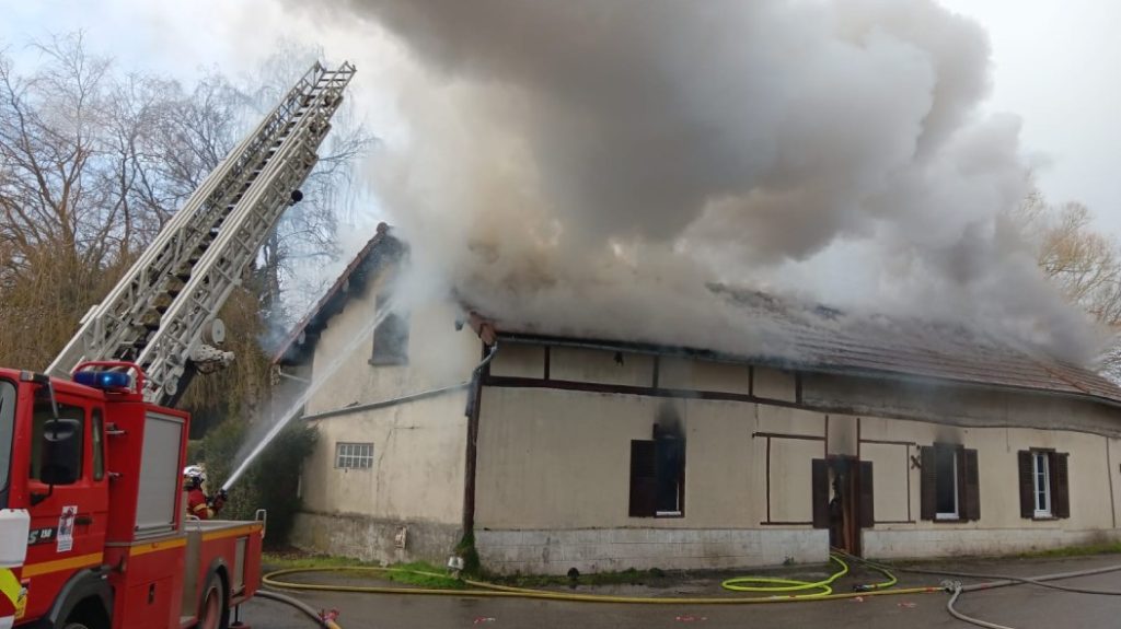 Photo of the building from which escapes a thick gray smoke. The fire truck with the deployed scale is visible to the left of the image.